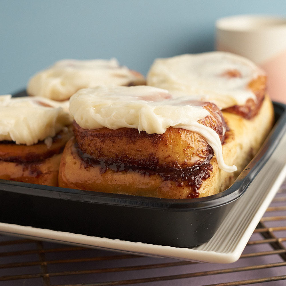 Photo of 4 cinnamon rolls in a tray, with icing dripping from the top of each roll.